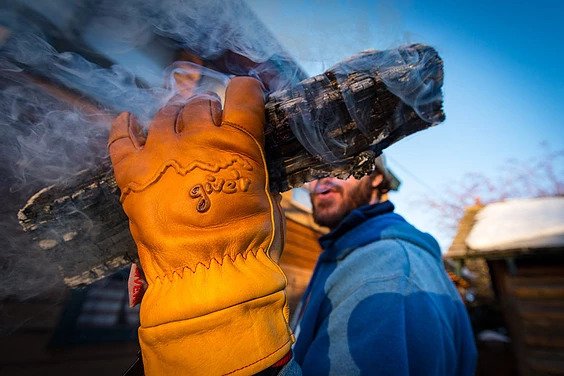 A man holds a smoking log while wearing fireproof gloves