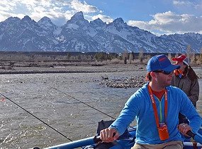 A man rafts on the snake river with the Grand Tetons in the background